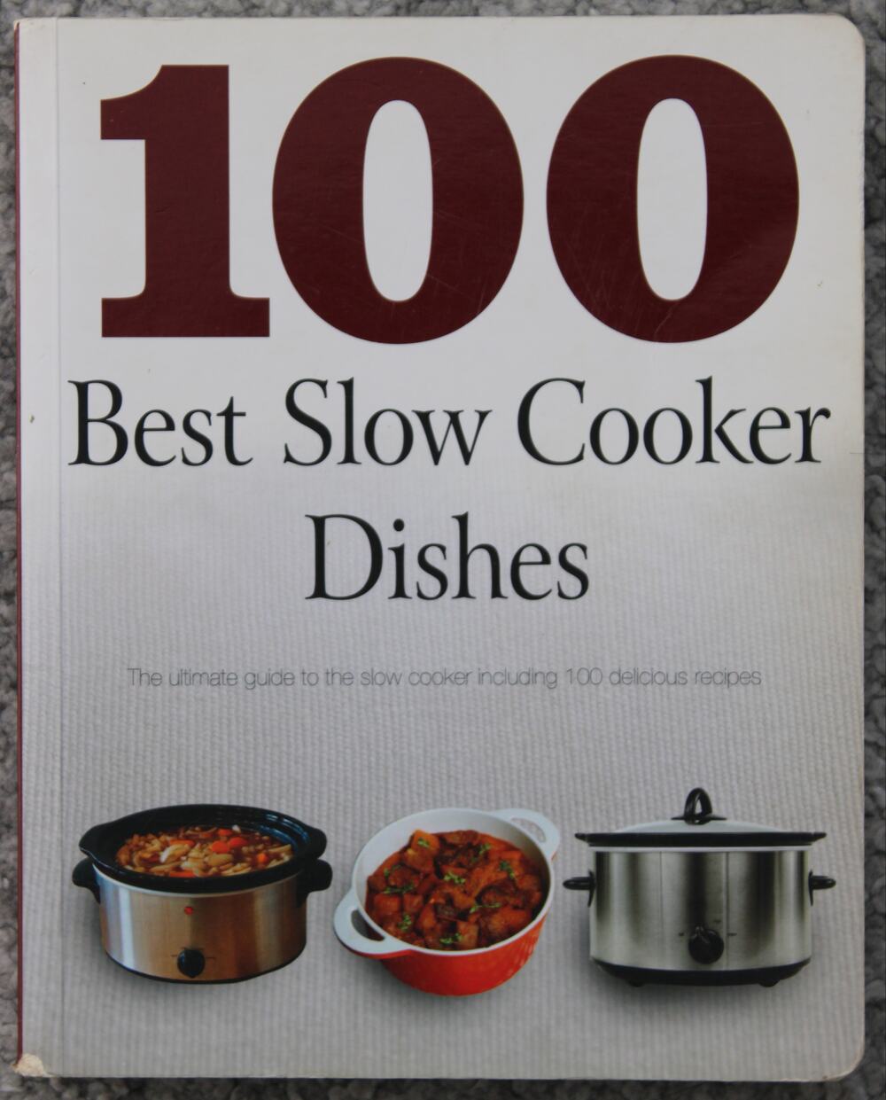 100 Best Slow Cooker Dishes cookbook with white cover and burgundy title